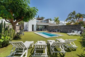 A pool area with white lounge chairs, a tree, and a stone wall.