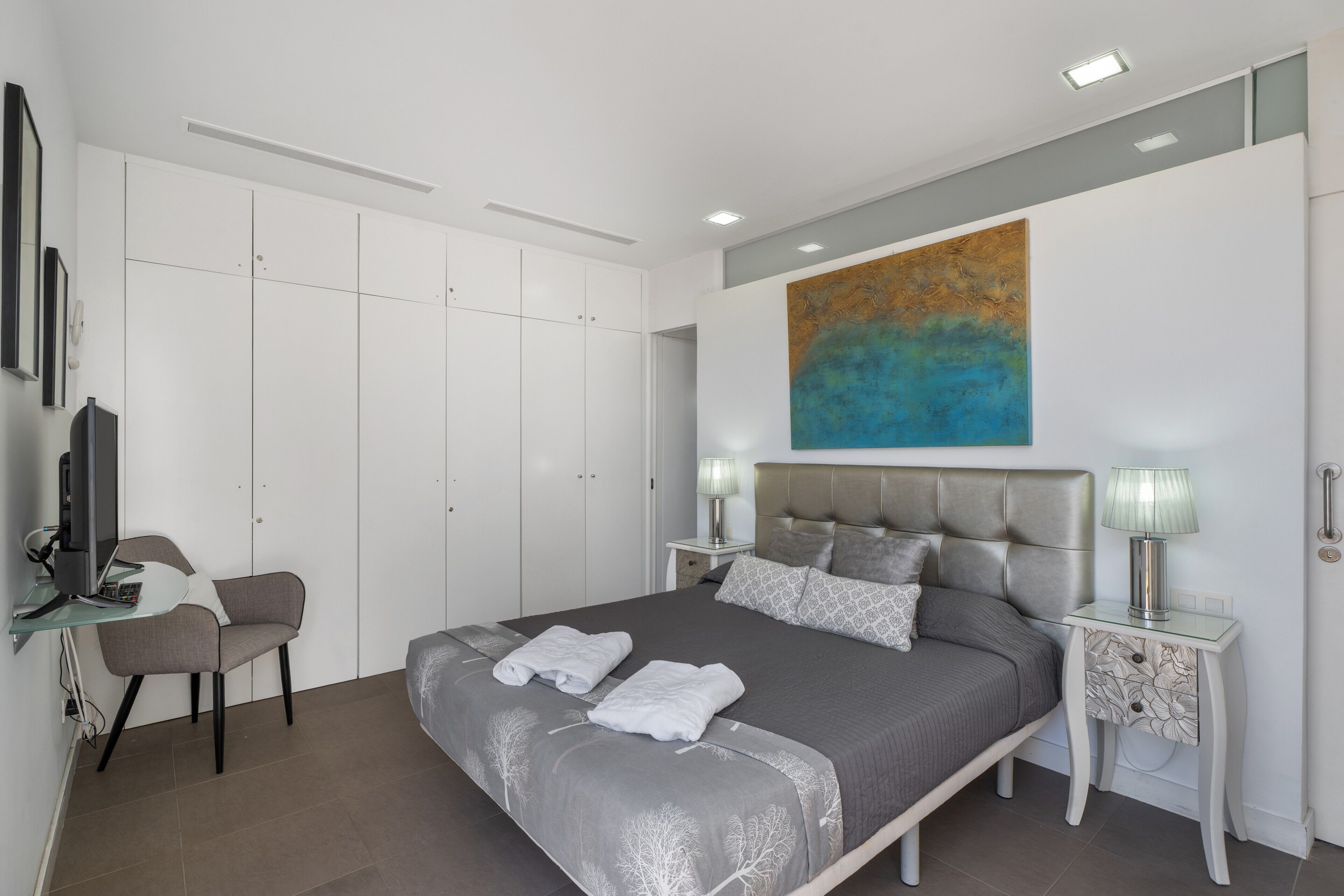 Ein modernes Schlafzimmer mit einem Bett, Nachttischen, einem Sessel und einem großen abstrakten Gemälde an der Wand.