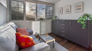 Ein modernes Wohnzimmer mit einer Couch, einem Couchtisch, einem Schrank und einem großen Fenster mit Blick auf Himmel und Wolken.