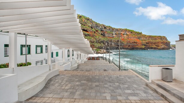 Eine Uferpromenade mit weißen Gebäuden, einer Treppe und Blick auf das Meer und die Klippen.