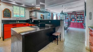 A kitchen with a central island, red cabinetry, and a bookshelf filled with books. - Bed and Breakfast 'La Pompadour' with Shared Pool, Shared Garden and Wi-Fi (Le Fraysse)