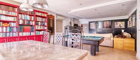 Una habitación amplia con mesa de billar, una mesa de comedor y una amplia estantería llena de libros.