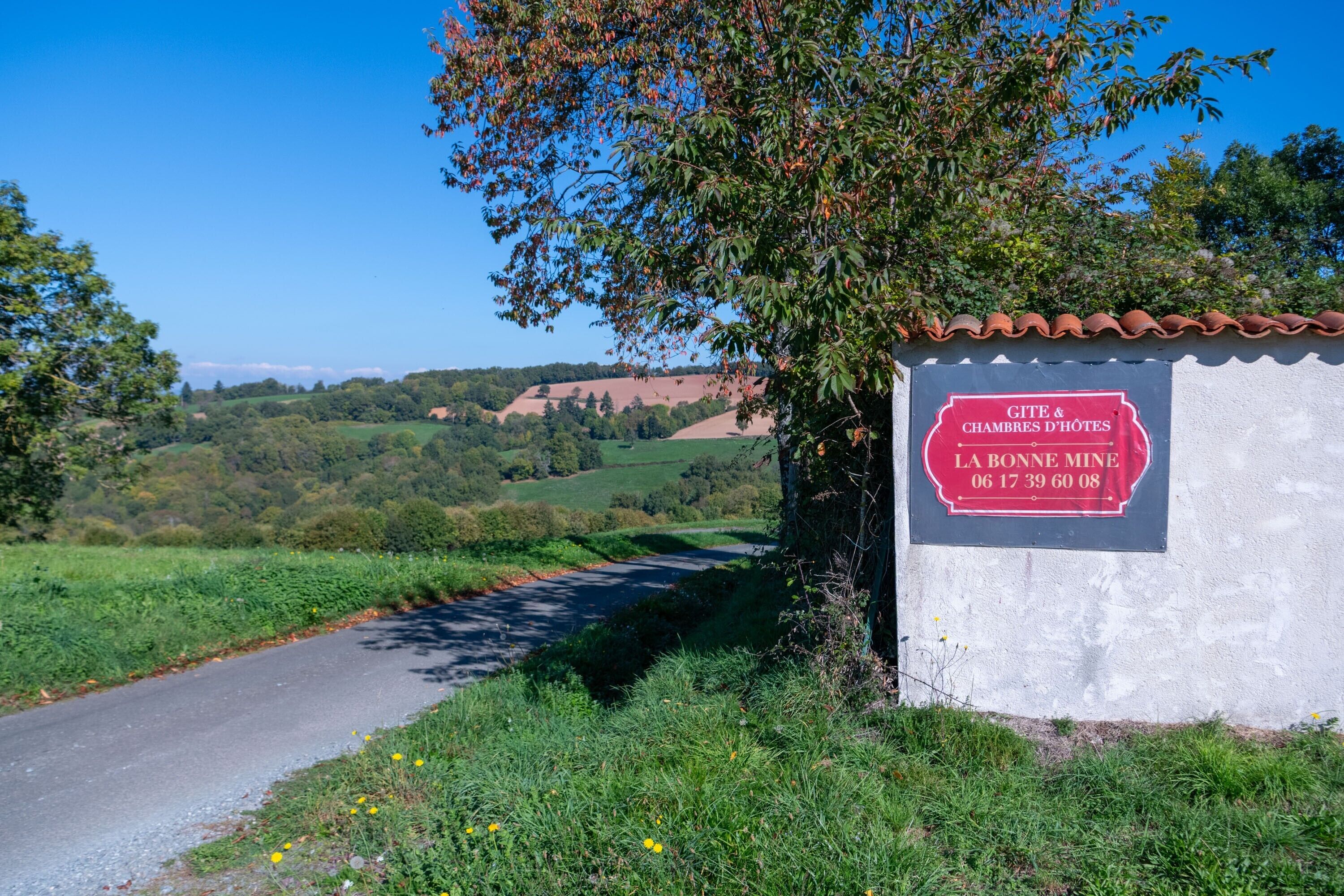 A rural road with a sign for 'GITE & CHAMBRES D'HOTES LA BONNE MINE 06 17 39 60 08.'