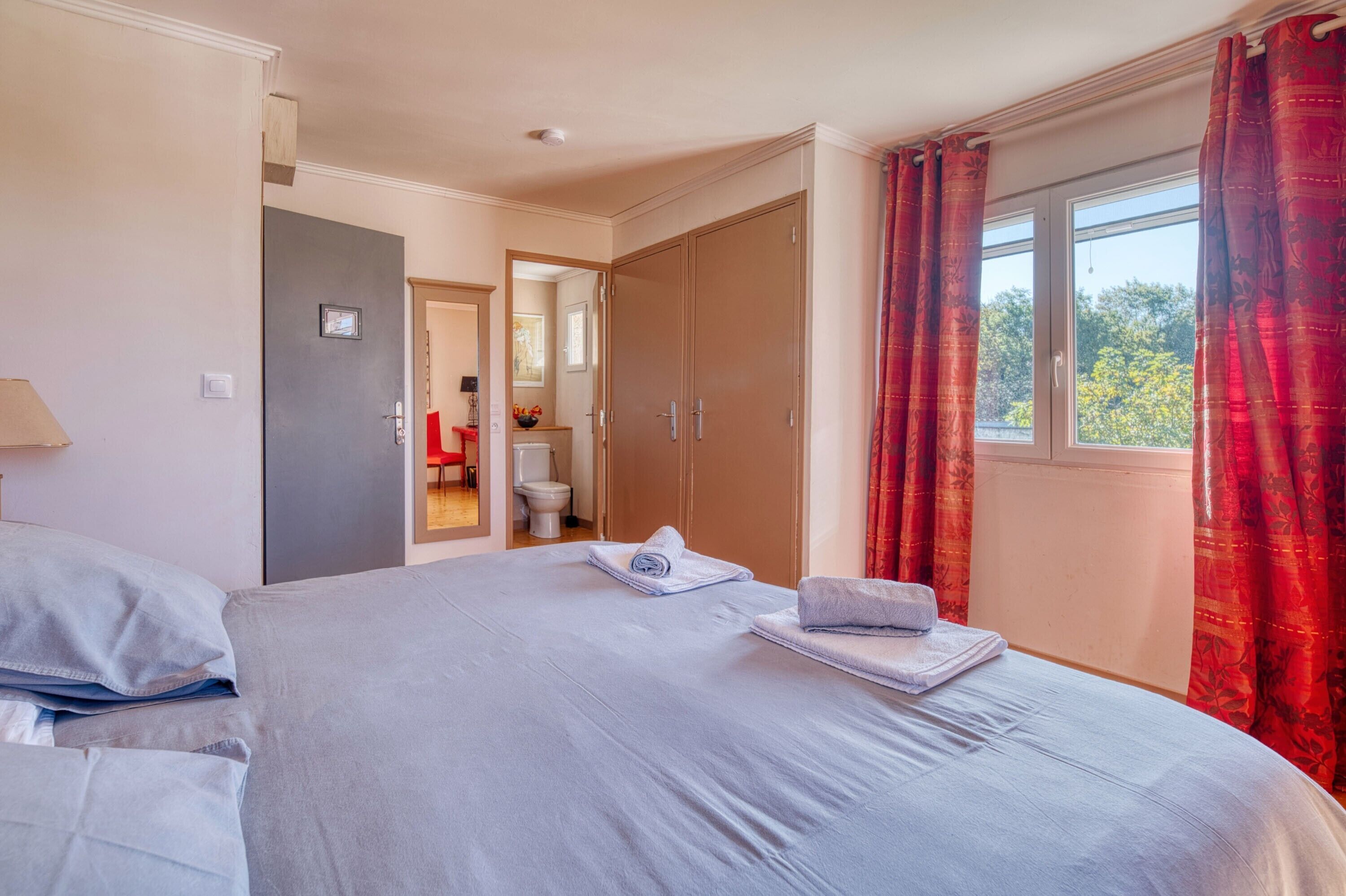 Une chambre d’hôtel avec un lit, une salle de bain visible à travers une porte ouverte et une fenêtre avec des rideaux.