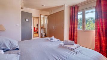 Une chambre d’hôtel avec un lit, une salle de bain visible à travers une porte ouverte et une fenêtre avec des rideaux.