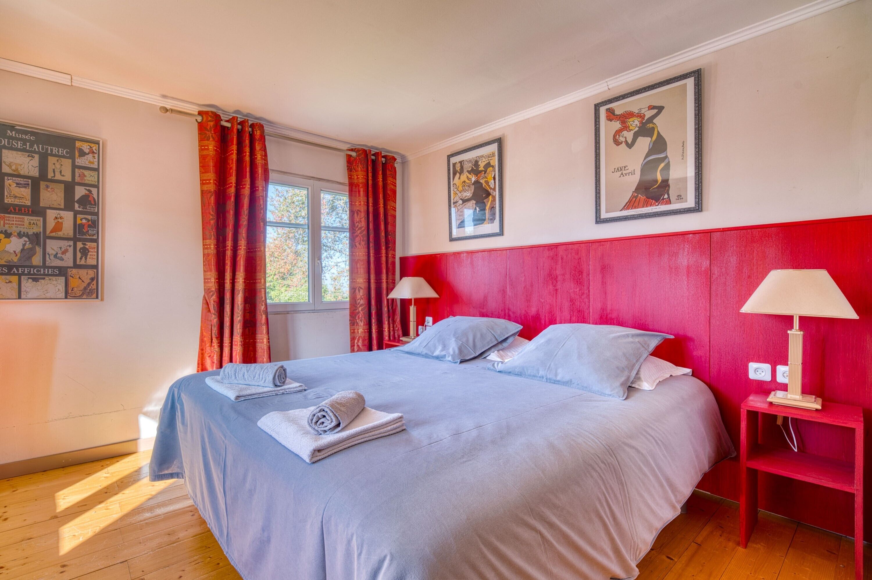 A room with a bed, two nightstands, a window with curtains, and wall art.