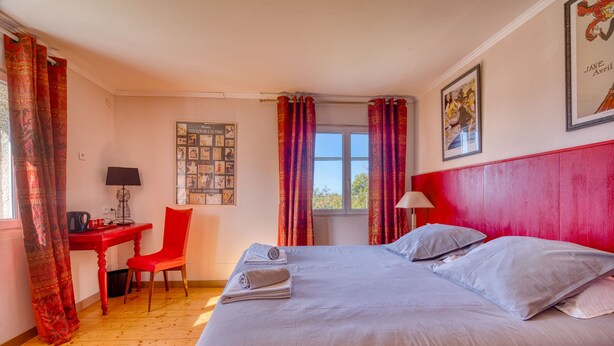 Una habitación de hotel con cama, escritorio, silla y ventana con cortinas.