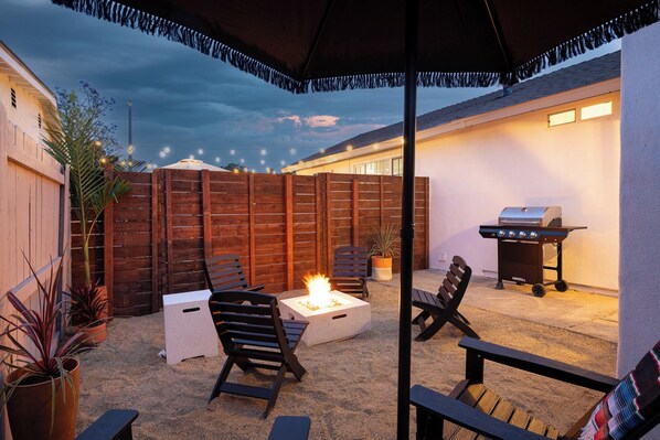 Patio con una fogata, mobiliario exterior y una parrilla.
