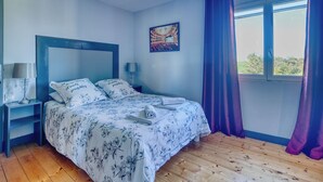 Ein Schlafzimmer mit einem Bett, Nachttischen, einem Fenster mit Vorhängen und einem Wandbild.