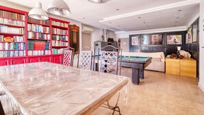 Ein geräumiges Zimmer mit Poolbillardtisch, Esstisch und einer großen Bücherwand voller Bücher.