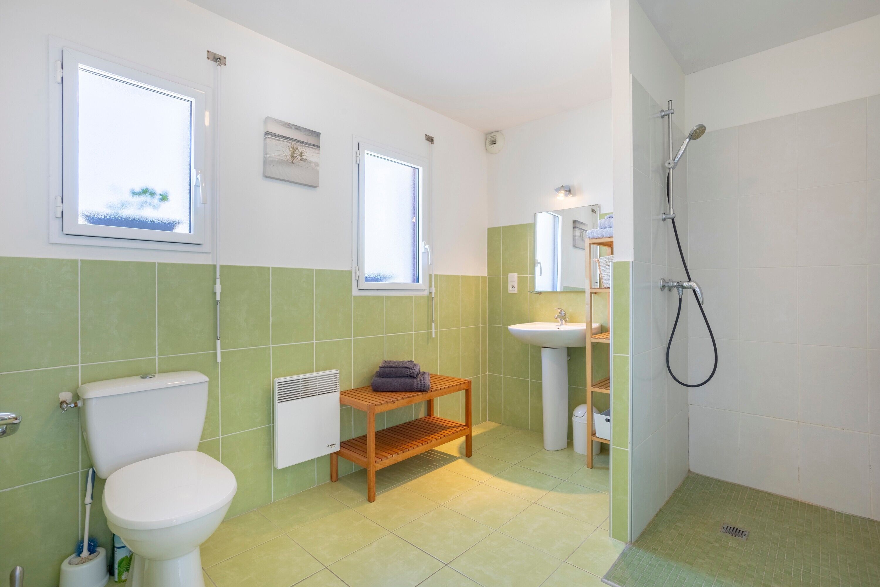 A bathroom with a toilet, sink, shower, and a window.