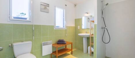 A bathroom with a toilet, sink, shower, and a window.