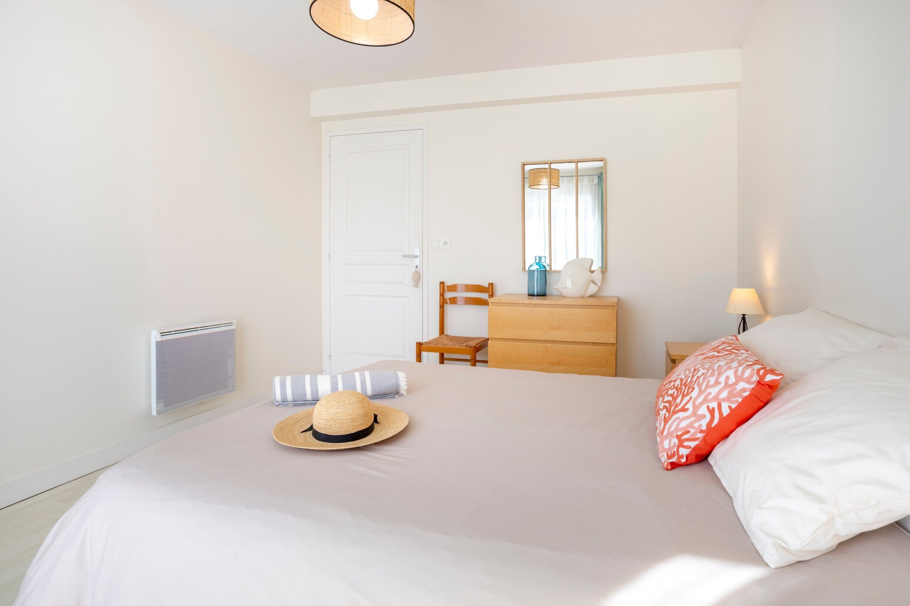 A bedroom with a bed, a dresser, a mirror, a radiator, and a hat on the bed.