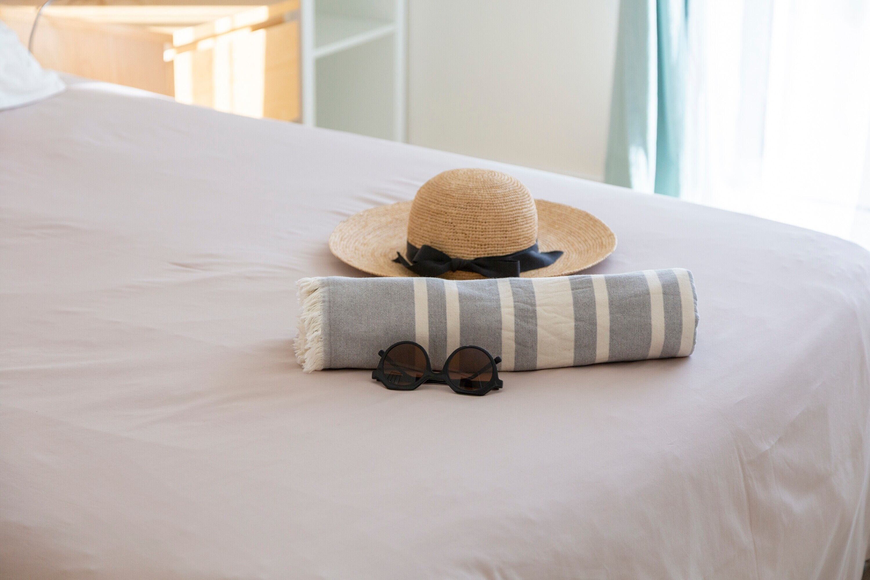 A bed with a striped pillow, a straw hat, and a pair of sunglasses.