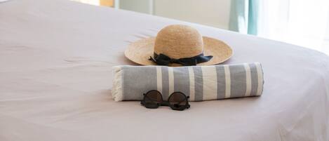 A bed with a striped pillow, a straw hat, and a pair of sunglasses.