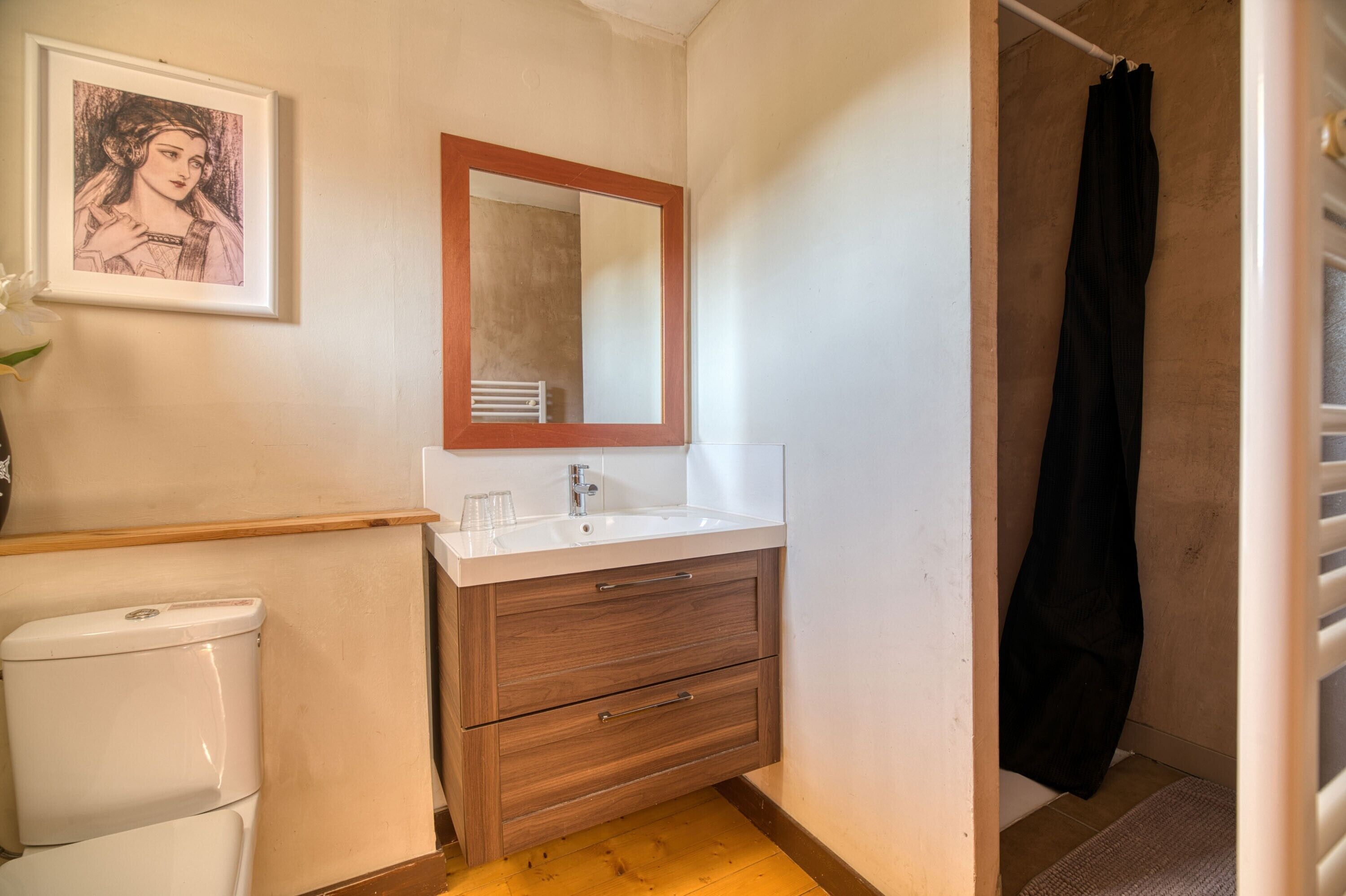 Ein Badezimmer mit Waschbecken, Holzschrank, gerahmtem Bild und schwarzem Duschvorhang.