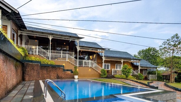 A swimming pool with a wooden deck and a covered outdoor area with stairs leading to a porch. - Johns Village  (Mulanthuruthy)