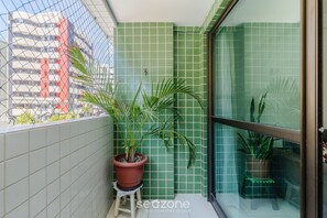 Ein Balkon mit grünen Fliesenwänden, Topfpflanzen und Blick auf ein Gebäude mit roten Akzenten.