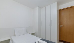 Ein kleines Zimmer mit einem Einzelbett, einer Holztür und weißen Wänden.