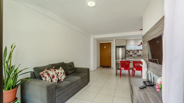 A living room with a grey sofa, a potted plant, and a kitchen area with red chairs and a refrigerator. - 2 Bedroom Apartment 700 m From the Beach Mbr0108 (Maceió)