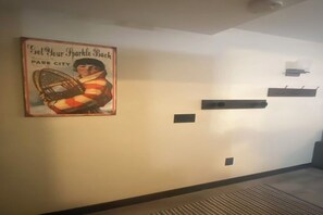 A hallway with a vintage poster, a vent, and a black shelf.