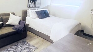 A small, modern room with a bed, a sofa, and a dining table. There is a framed picture of a deer on the wall.