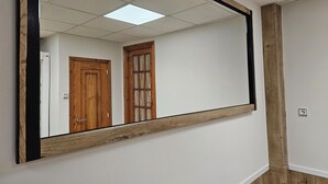 A large mirror with a wooden frame reflecting a room with a wooden door and a ceiling light. - Real 43 Casa Neda (neda)