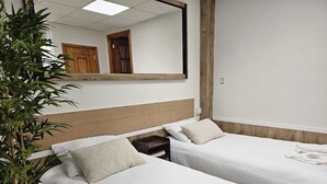 A hotel room with two single beds, a wooden headboard, a large mirror, and a bamboo plant. - Real 43 Casa Neda (neda)