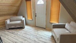 A loft bedroom with a sloped ceiling, two sofas, a door with a star-shaped window, and wooden flooring.