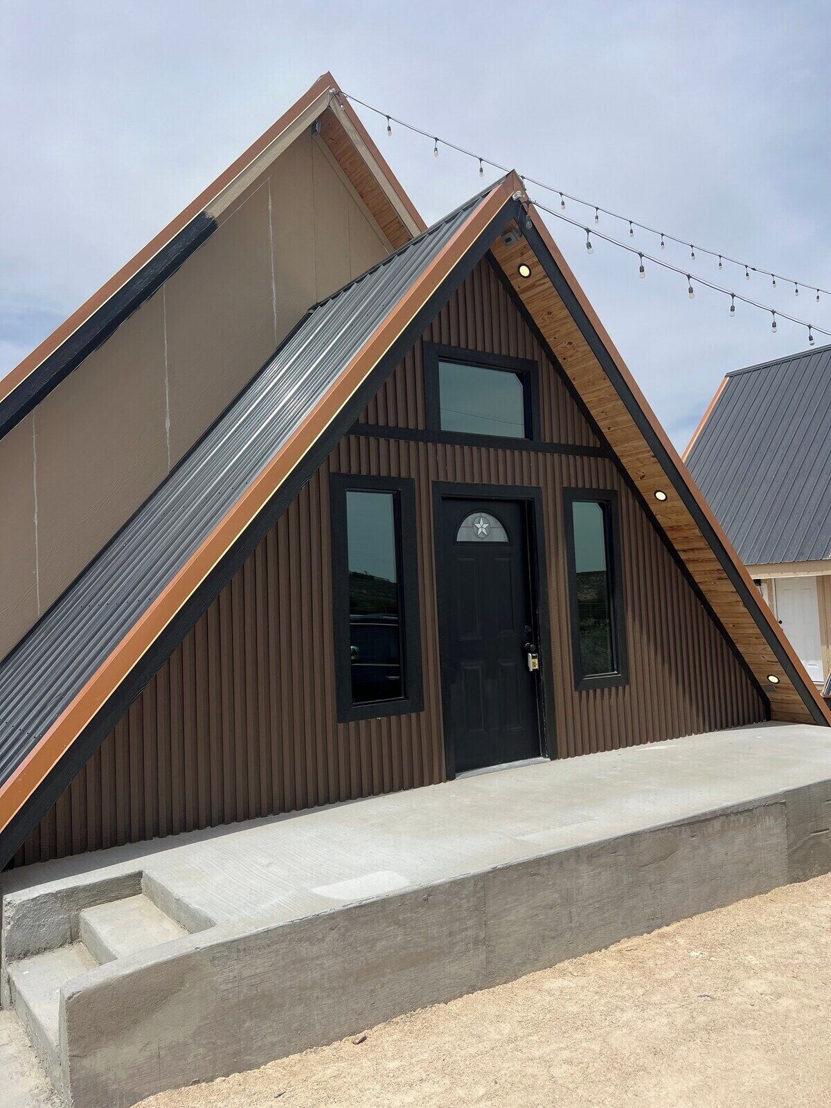 A modern building with a sloped roof, a black door, and a small set of concrete steps leading to the entrance.