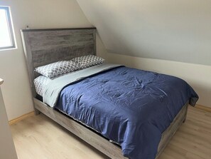 A single bed with a wooden headboard in a room with a sloped ceiling.