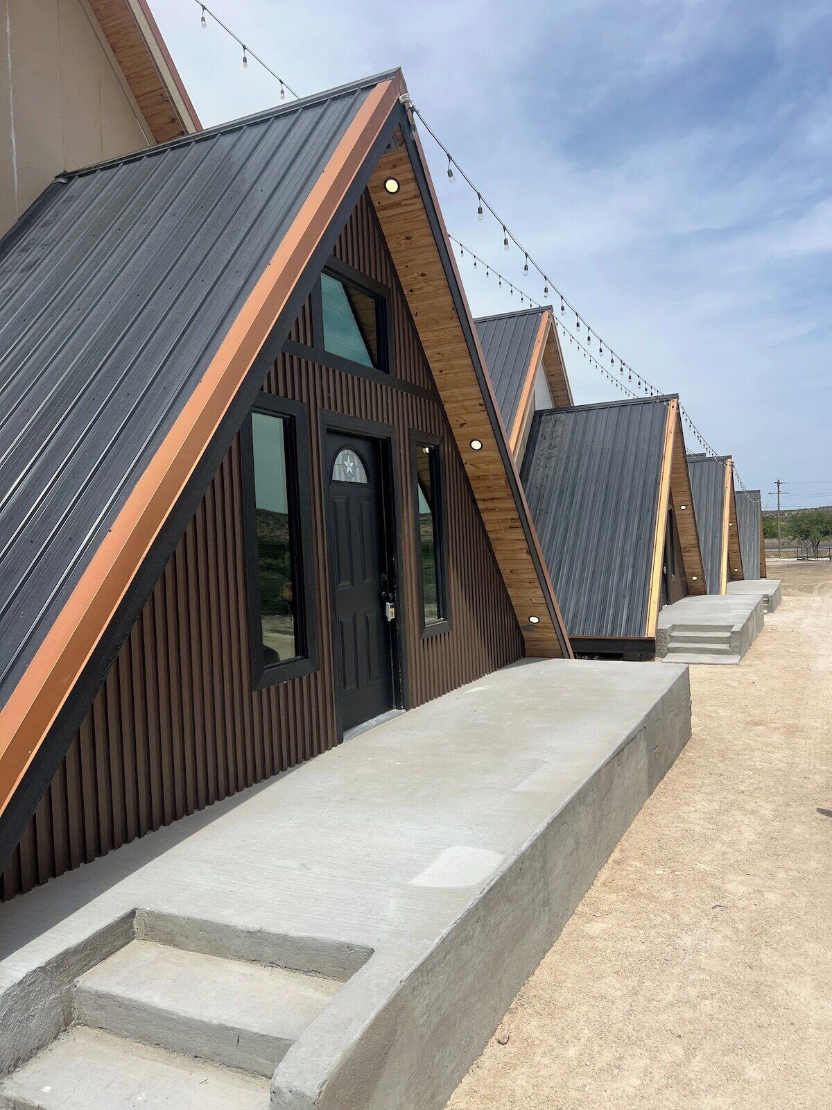 A row of modern, triangular-roofed cabins with concrete steps leading to the entrance.