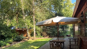 An outdoor patio with a table and chairs under a canopy, surrounded by a garden and trees. - Chaletpark Kempenbos - 196 (Diessen)
