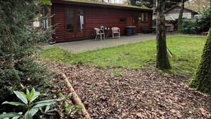 A rustic cabin with a covered patio, a small table and chairs, and a well-maintained lawn. - Chaletpark Kempenbos - 196 (Diessen)