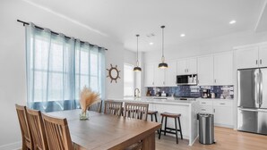 A modern kitchen with white cabinets, a stainless steel refrigerator, and pendant lighting.