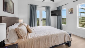 A bedroom with a bed, a TV, a ceiling fan, and a window with curtains.