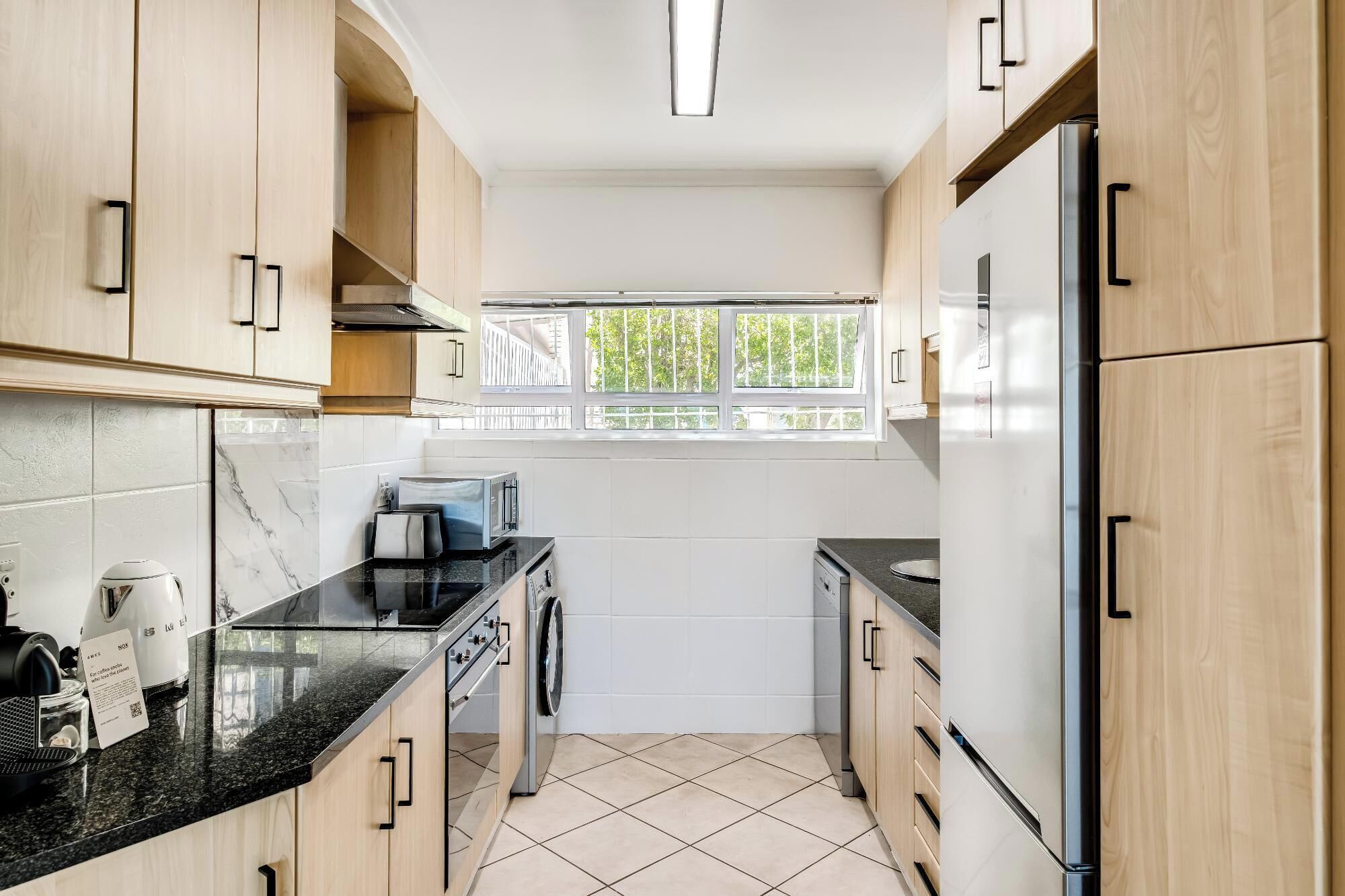 Een moderne keuken met houten kastjes, een zwart aanrecht, een ingebouwde oven, een magnetron en een koelkast.