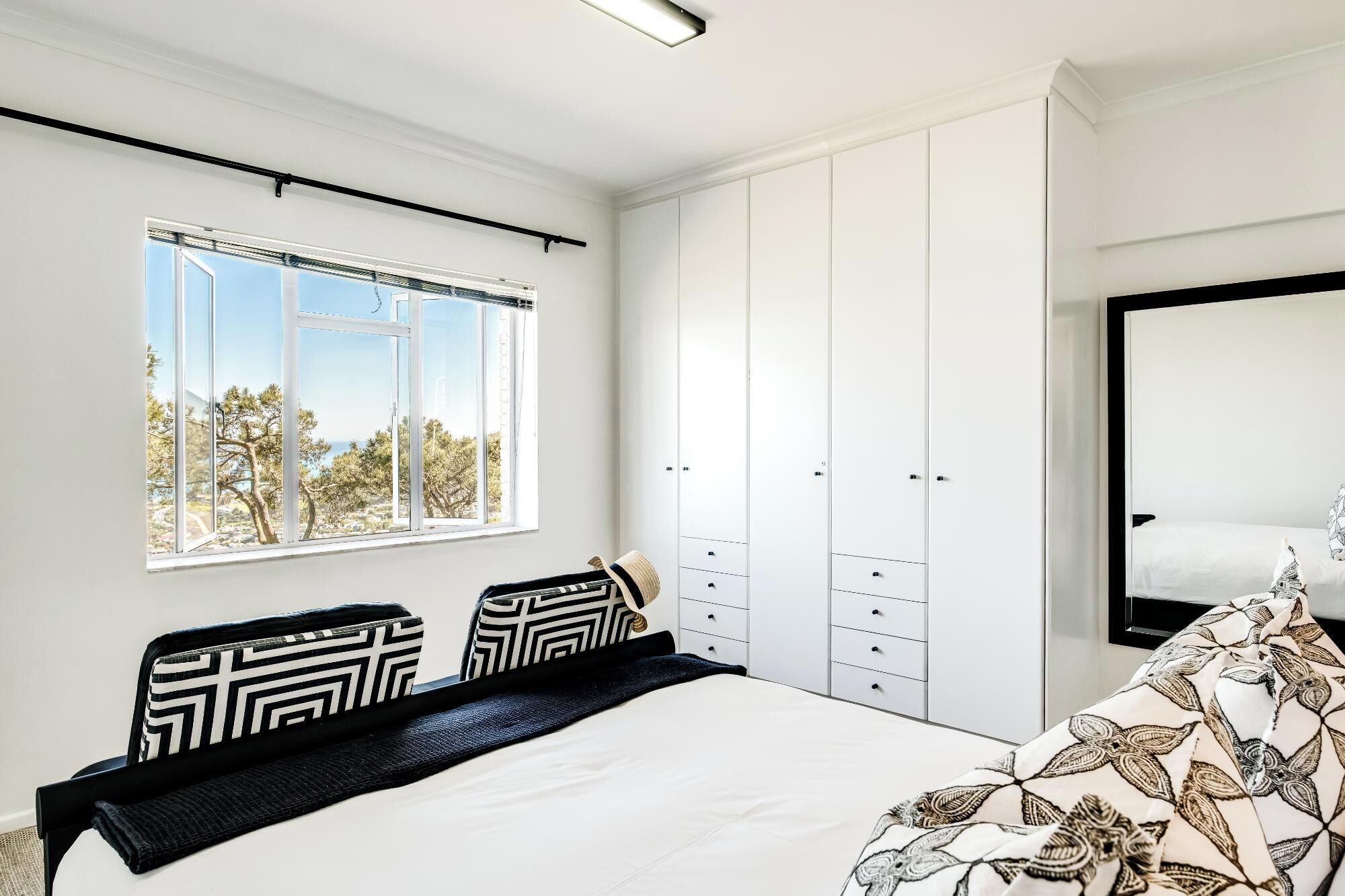 A bedroom with a bed, a wardrobe, a window with a view, and a mirror.