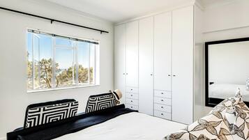 A bedroom with a bed, a wardrobe, a window with a view, and a mirror.