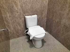 A toilet with a white tank and lid, a flush handle, and a towel on the seat. - Alit Guest House (Jimbaran)