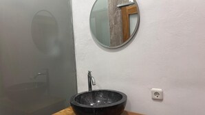 Casa de banho com espelho redondo, lavatório preto e bancada de madeira.