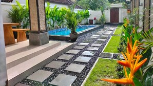 Uma área de piscina com um caminho de pedra, plantas em vasos e um banco.