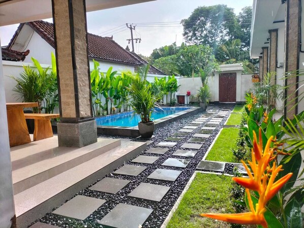 A pool area with a stone pathway, potted plants, and a bench. - Alit Guest House (Jimbaran)
