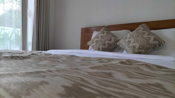 Uma cama com colcha estampada, cabeceira de madeira e duas almofadas estampadas.
