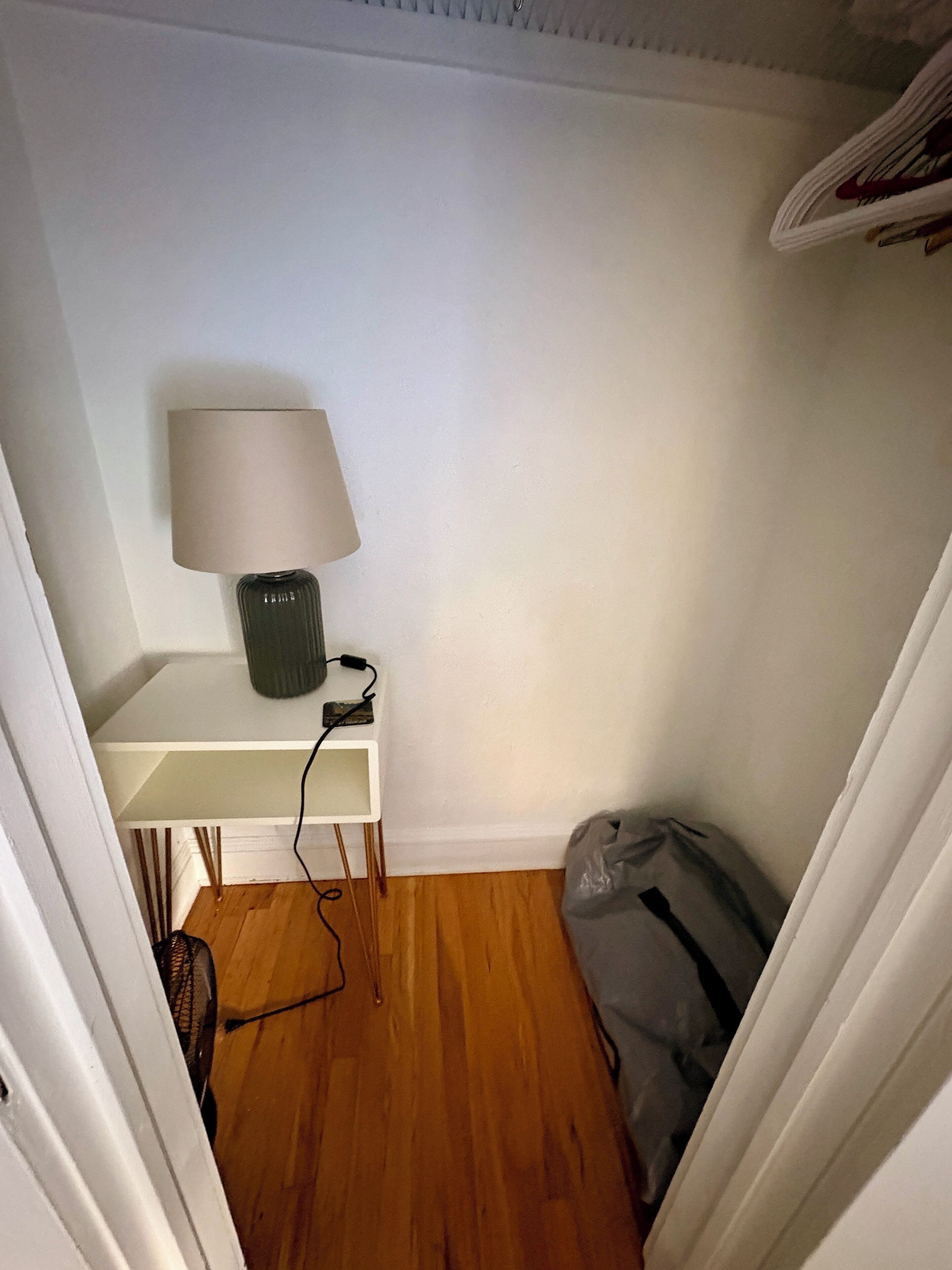 Een kleine kamer met een wit bureau, een lamp en een tas op de vloer.