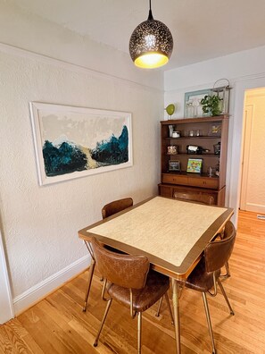 Ein Essbereich mit Tisch, Stühlen, einer Pendelleuchte, einem Bücherregal und einem gerahmten Gemälde an der Wand.