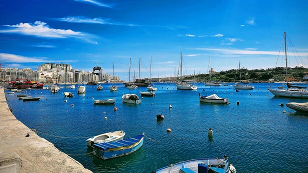 A marina with numerous boats docked, a city skyline in the background, and a clear blue sky. - Designer Penthouse by the Promenade | BBQ Terrace (Gzira)