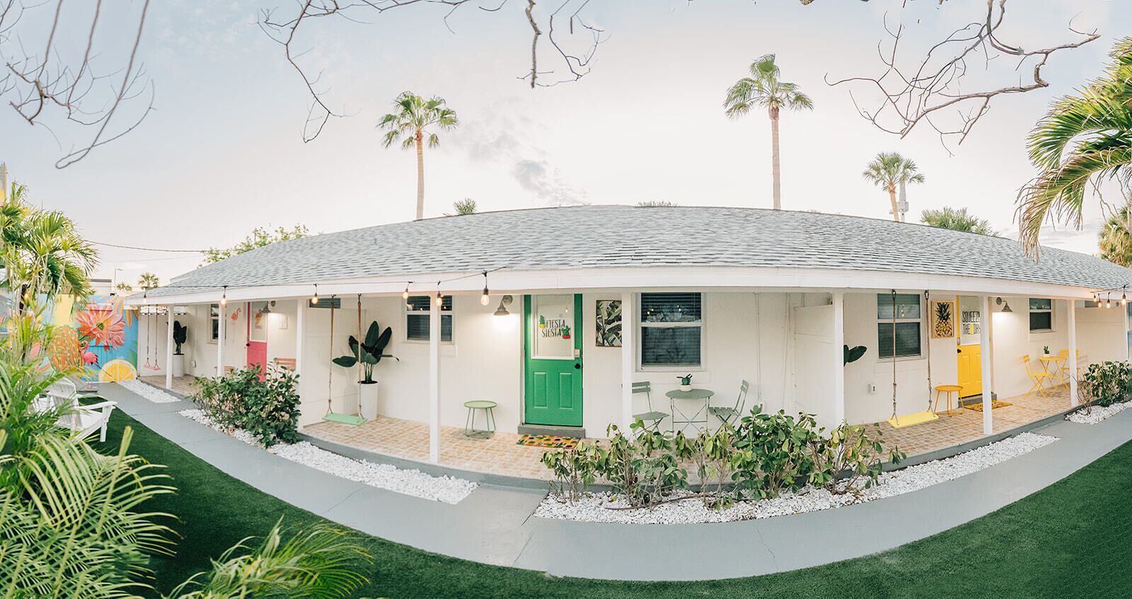 A circular building with a green door, outdoor seating, and palm trees.