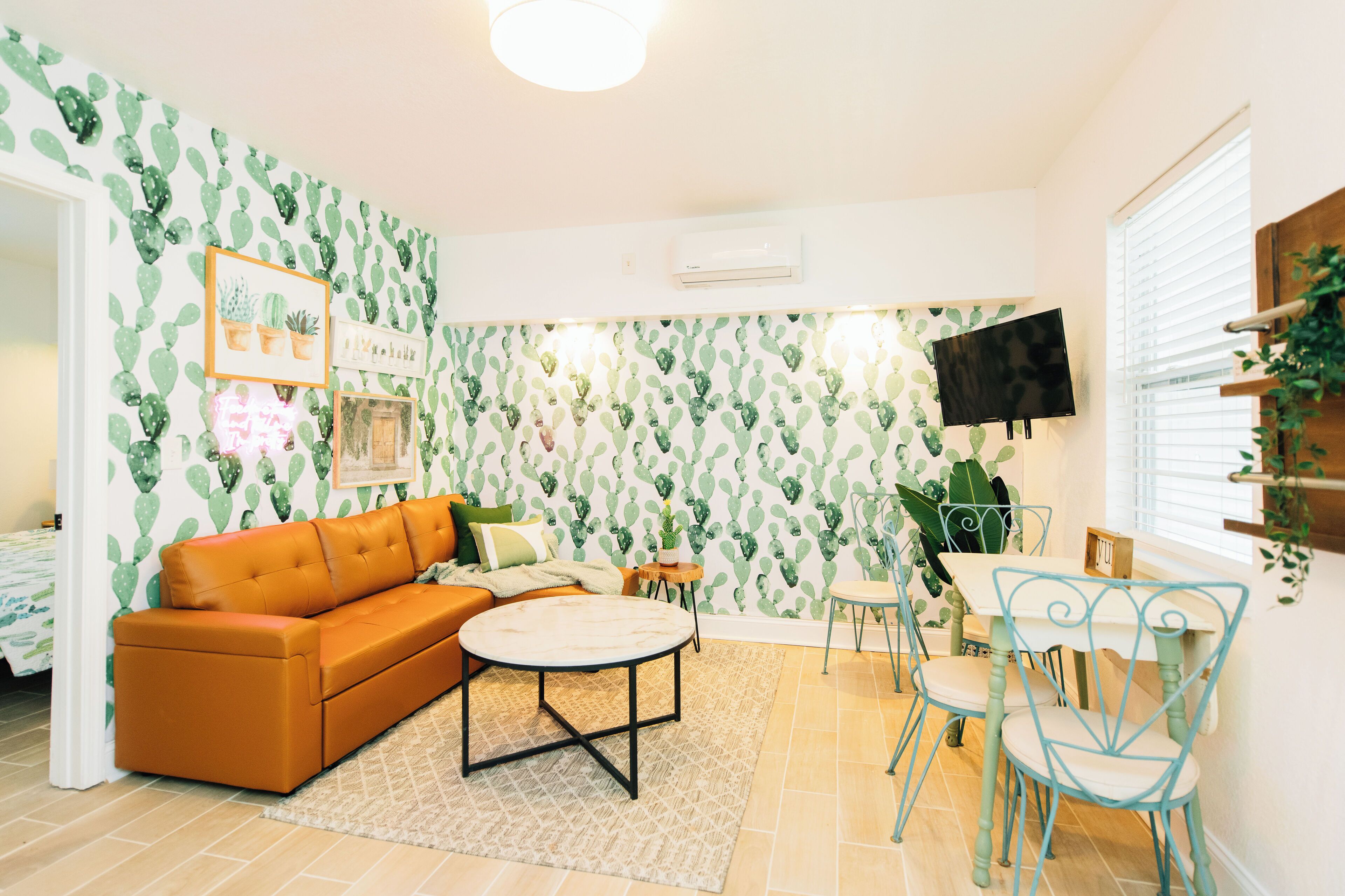 Un salon avec un papier peint à motifs de cactus, un canapé marron, une table basse ronde et un coin repas avec une table et des chaises.