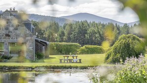 Een gebouw van steen met een picknicktafel en een vijver in een aangelegde tuin.